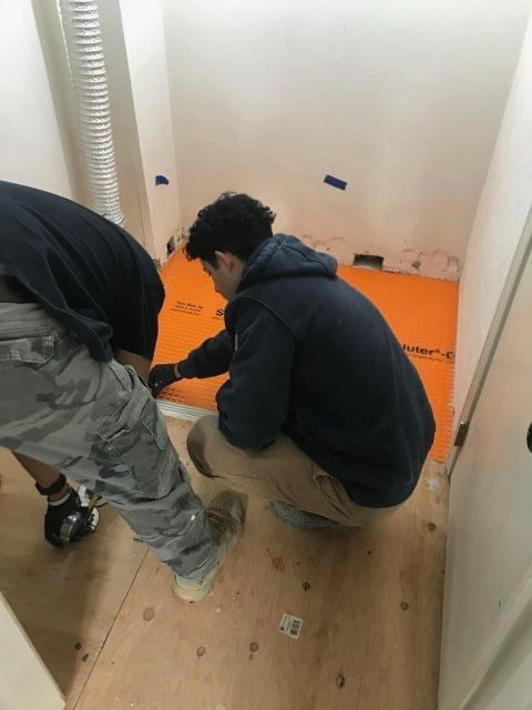 Two men are working on a wooden floor in a room.