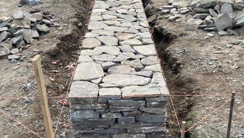 A stone wall is being built in the dirt.