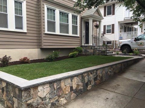 A house with a stone wall and a truck parked in front of it.