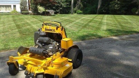 A yellow lawn mower is parked in a driveway next to a lush green lawn.