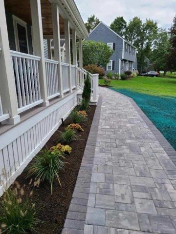 A brick walkway leading to a house with a porch.