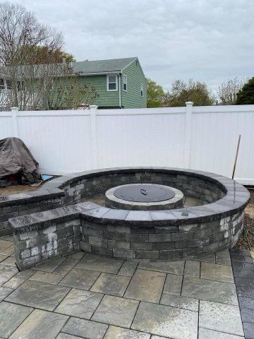 A fire pit is being built on a patio next to a white fence.