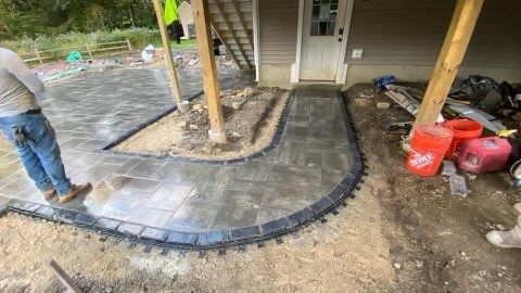 A man is standing next to a concrete walkway in front of a house.