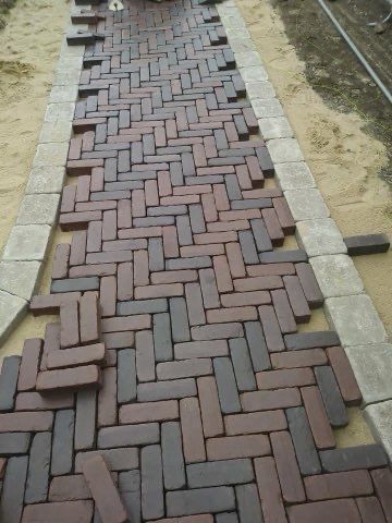 A brick walkway is being built in a herringbone pattern