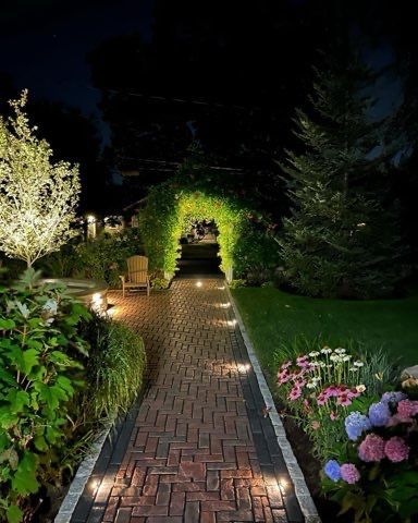 A brick walkway is lit up at night in a garden.