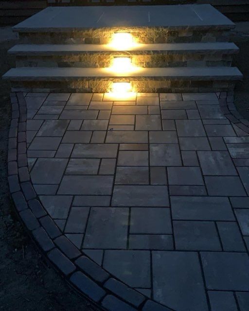 A brick walkway with lights on the steps at night.