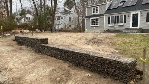A large stone wall is being built in front of a house.