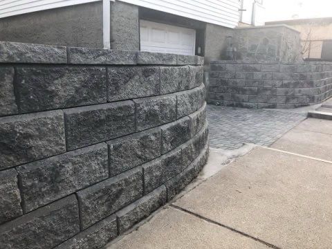 A brick wall is surrounding a driveway and garage next to a house.