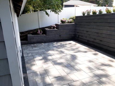 A patio with a brick wall and a white fence in the background.