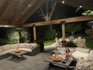 A woman is sitting on a couch under a covered patio at night.