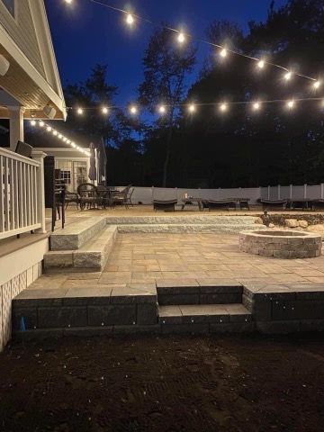 A patio with a fire pit and stairs is lit up at night.