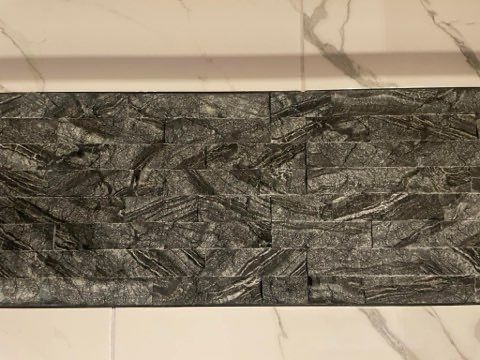 A close up of a black tile on a marble wall.