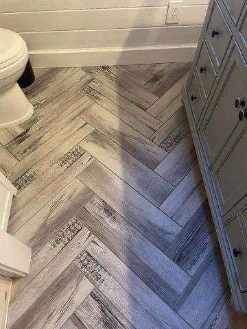 A bathroom with a herringbone tile floor and a toilet.