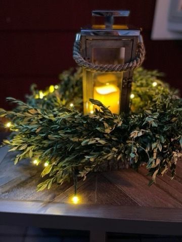 A lantern is sitting on top of a wooden table next to a wreath.