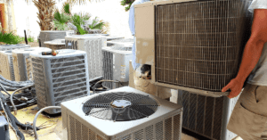Man holding an air conditioning unit among several others on a patio.