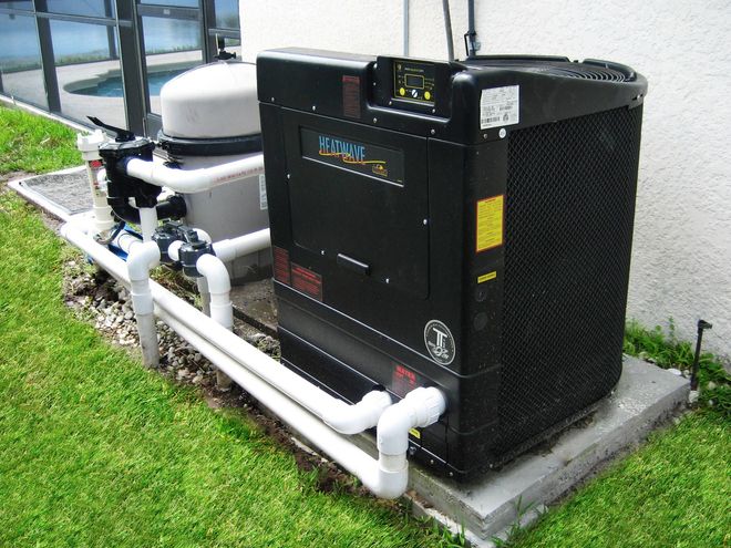 Pool pump and heater system outside near grass. White pipes connect to a black unit and a filter.