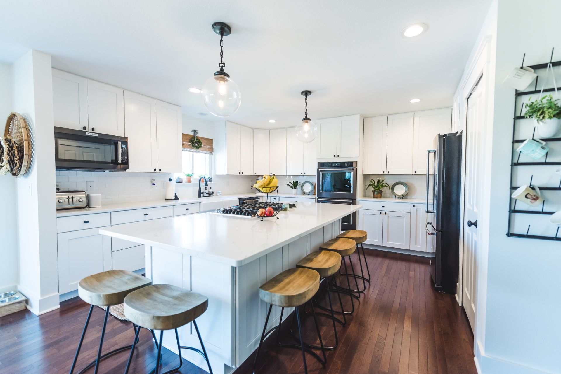A kitchen with white cabinets , wooden floors , stools and a large island.
