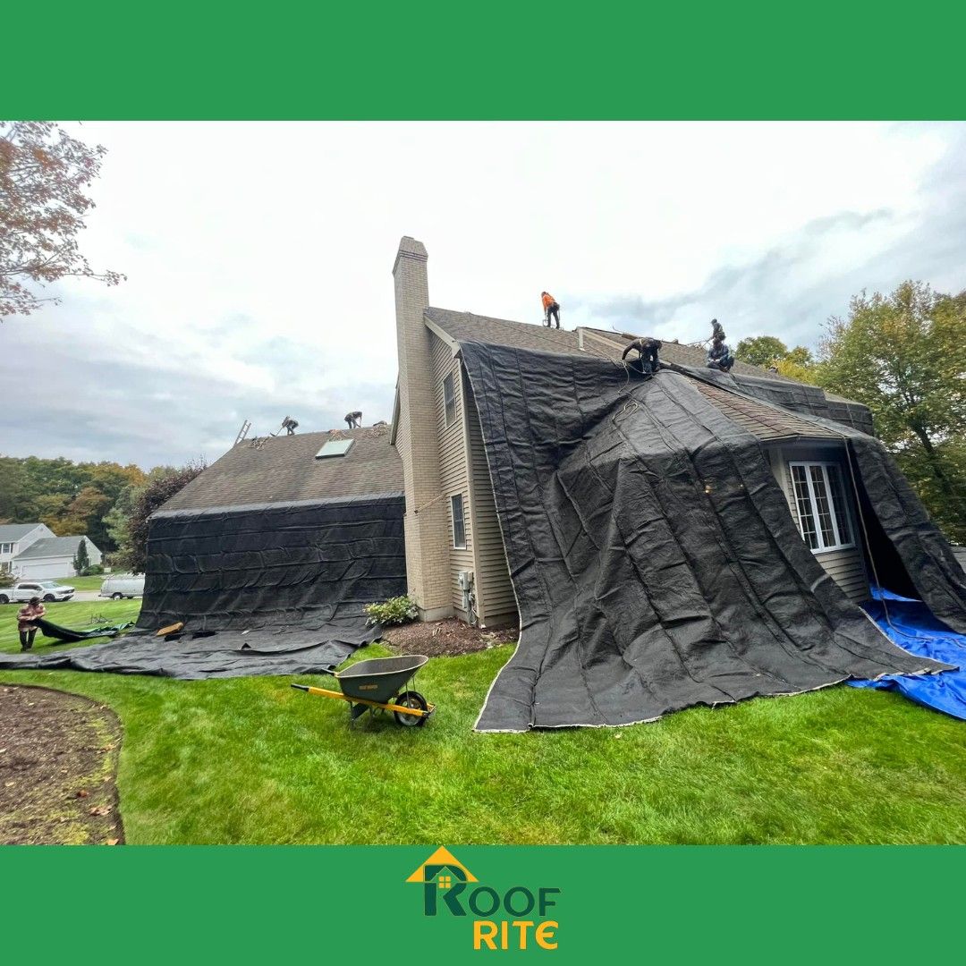 Roof covered with black tarp; workers on roof, green lawn, cloudy sky.