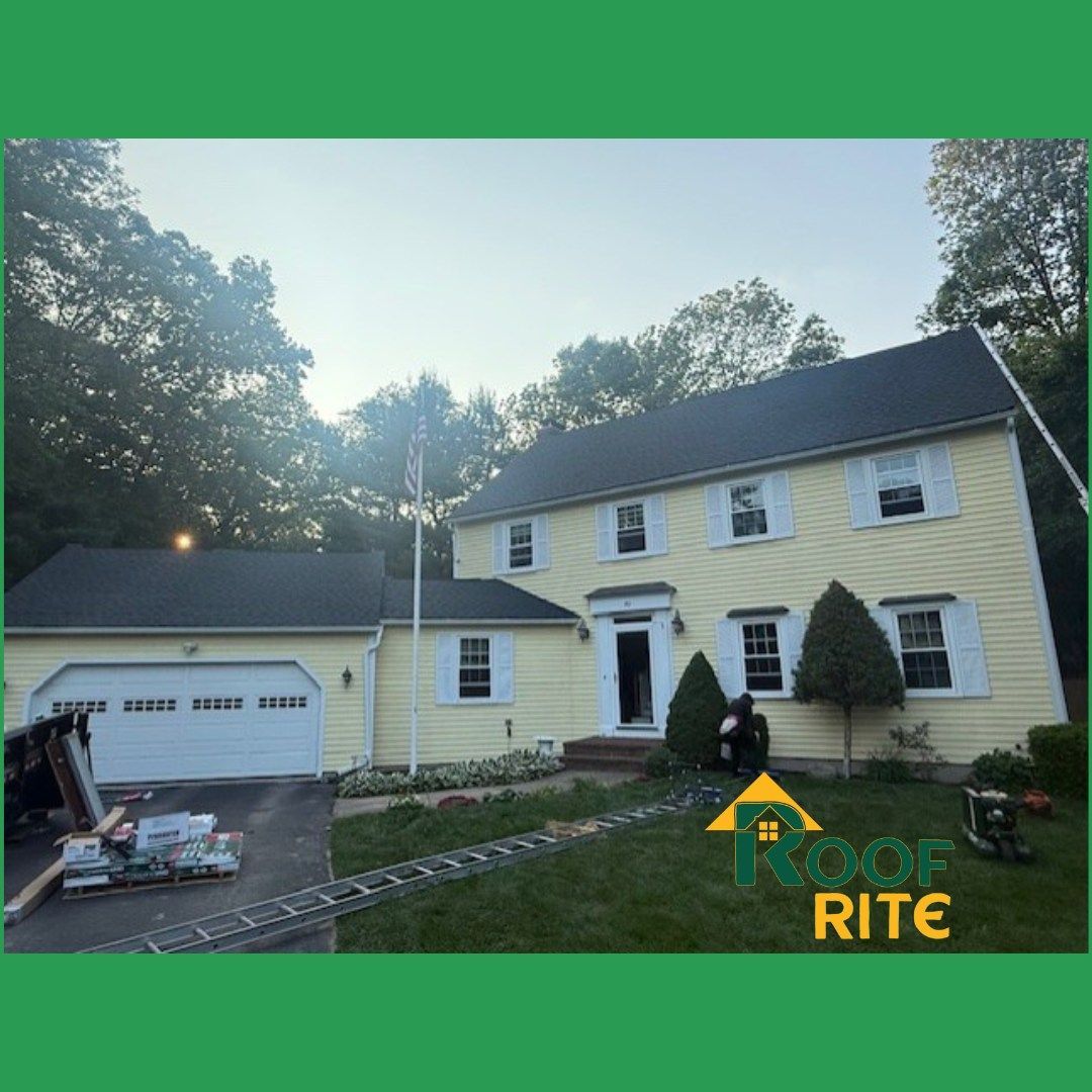 Yellow house with black roof, white trim. Workers by front door. Green grass, trees in background.