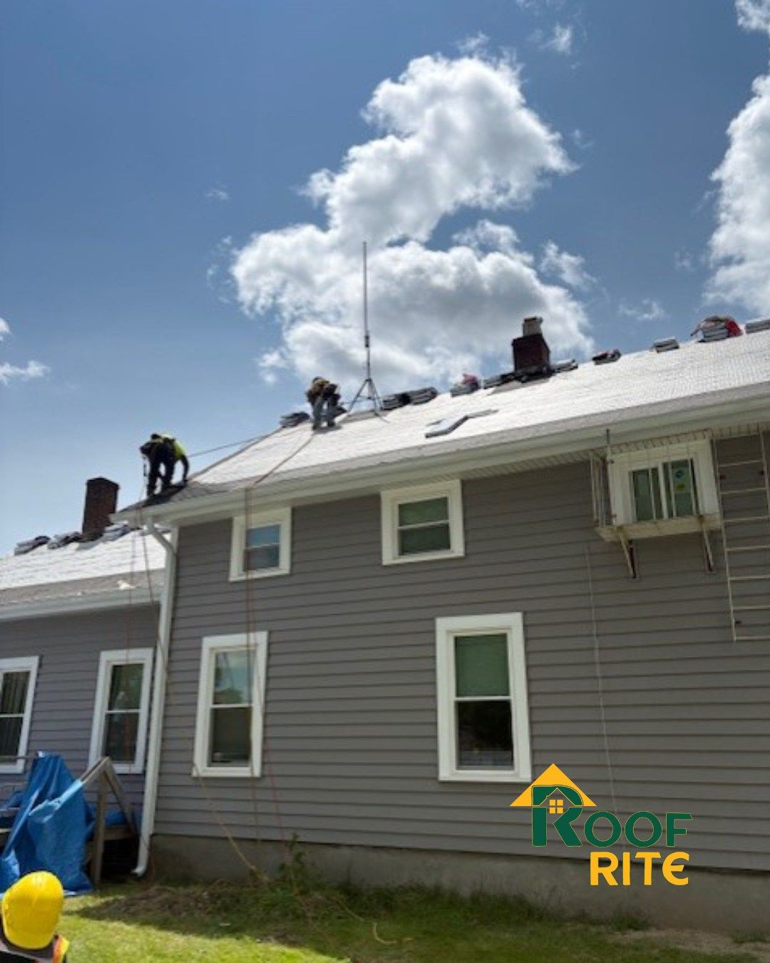 Roofers on a gray house with a blue sky, working on the roof.
