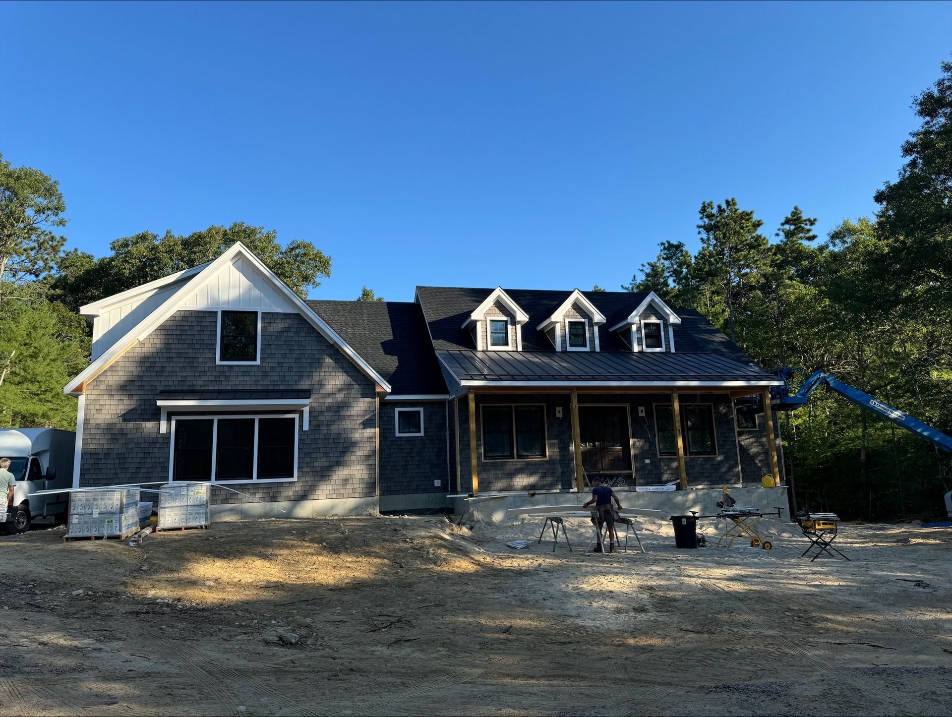 New home under construction with gray shingles, dormers, and porch.