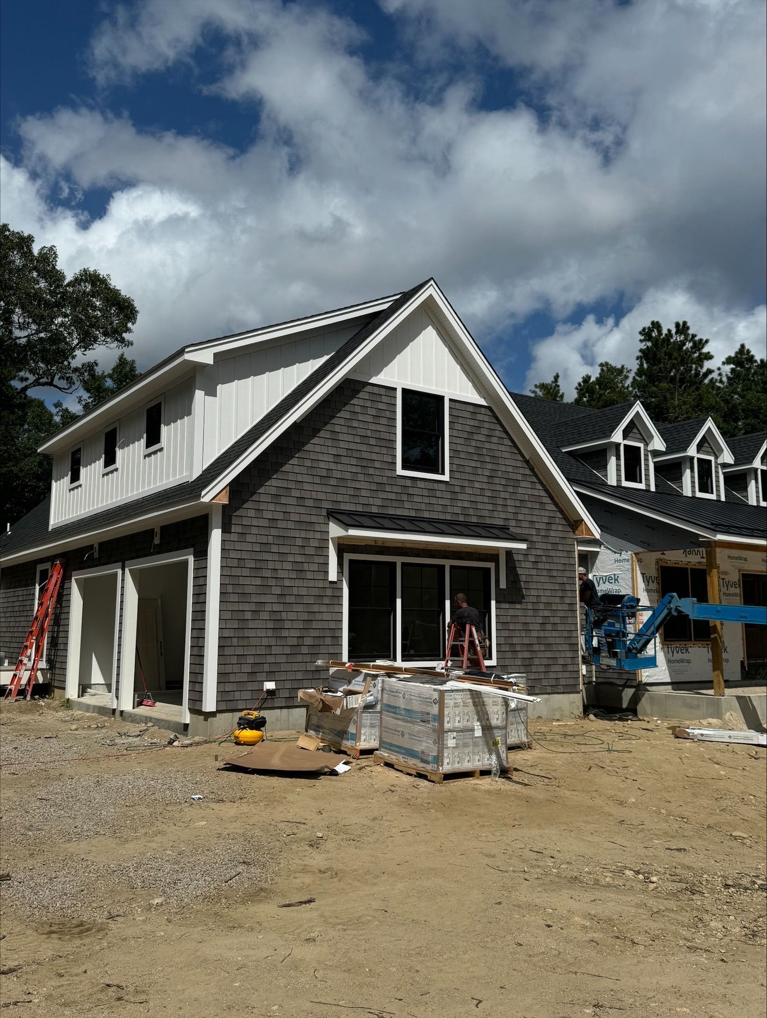 Building under construction, gray shingle siding, white trim, glass sliding door, cloudy sky.
