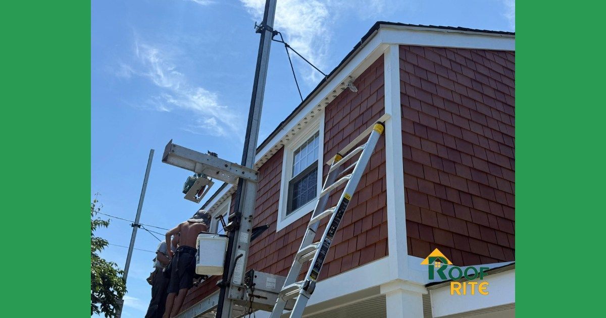 Construction worker on a ladder repairing the exterior siding of a brown and white building. Clear sky in background.