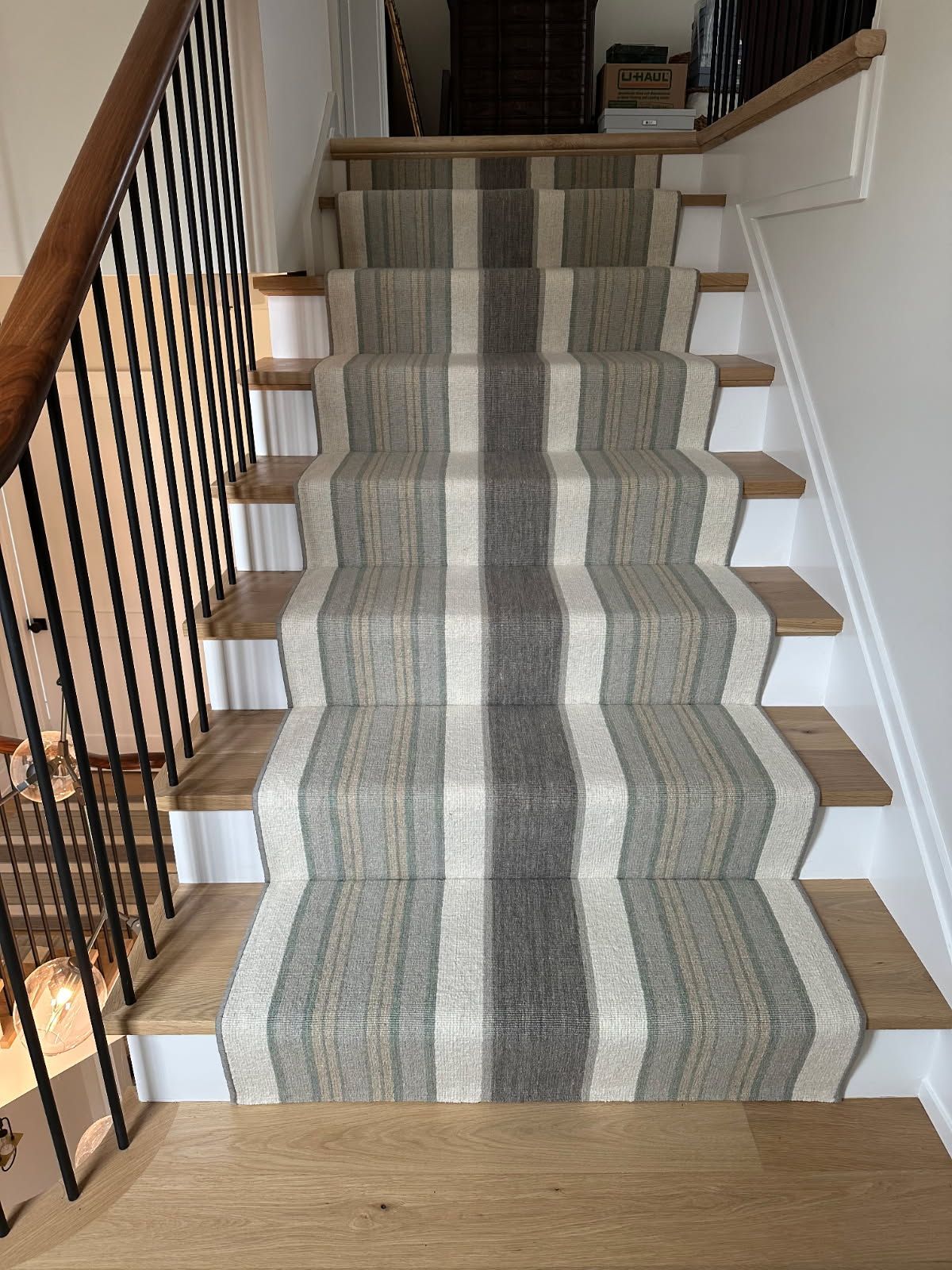 Staircase with striped carpet runner in neutral tones, wooden treads, and a black metal railing.