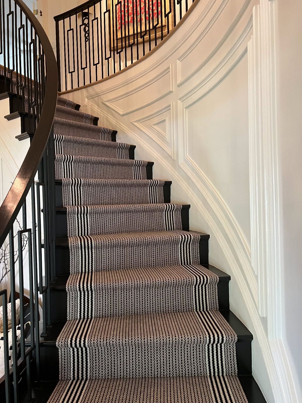 A curved staircase with black and white striped carpet, black railing, and white wall paneling.