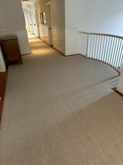 Hallway with light brown carpet, white walls, and a railing on the right.