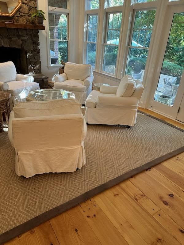 Living room with white slipcovered chairs, gray rug, wood floor, and large windows.