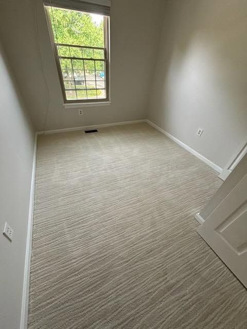 Empty room with light-colored carpet, gray walls, and a window.