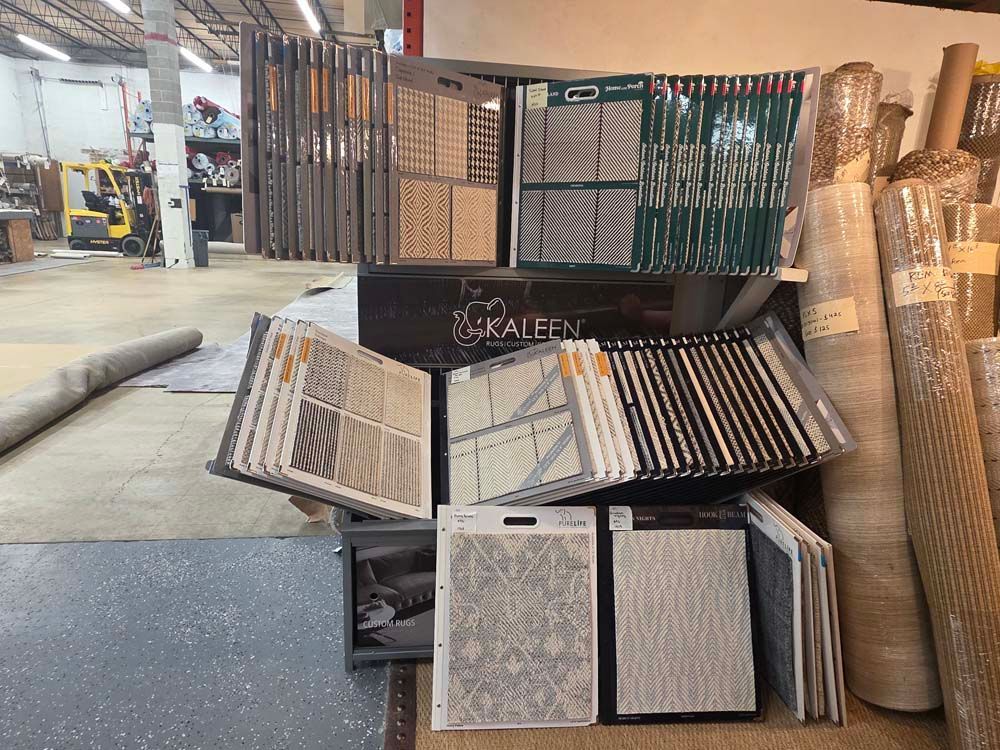 Display of carpet samples in a warehouse setting, with rolled carpets in the background.