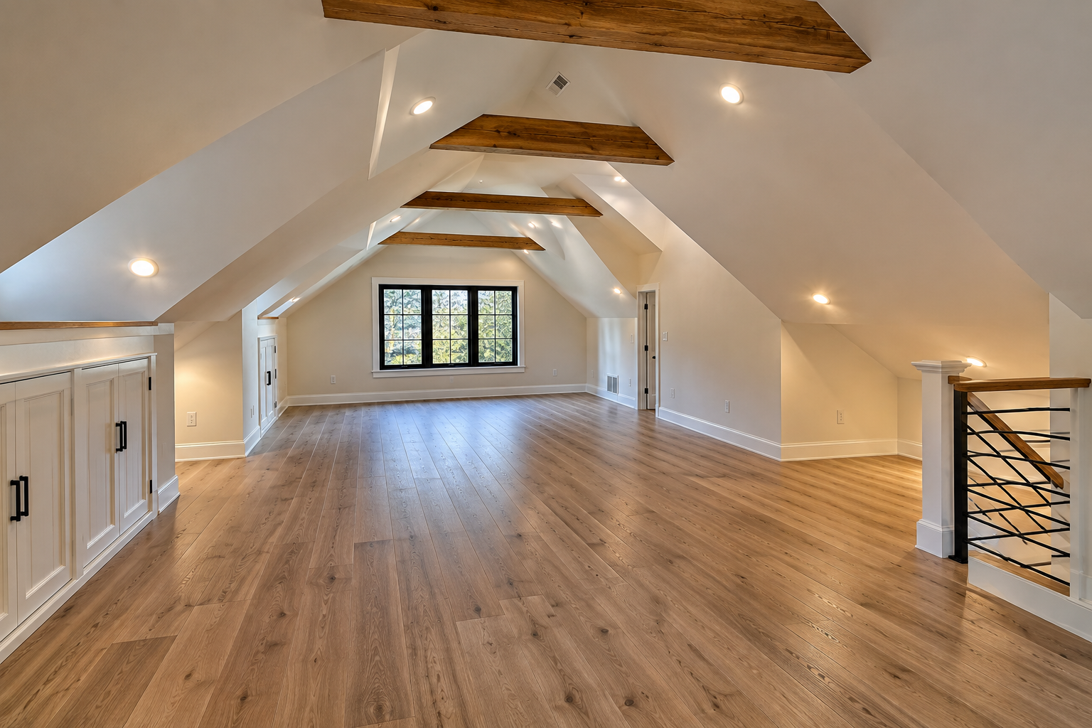 Bright empty attic room with hardwood floors, exposed beams, and a window at the far end