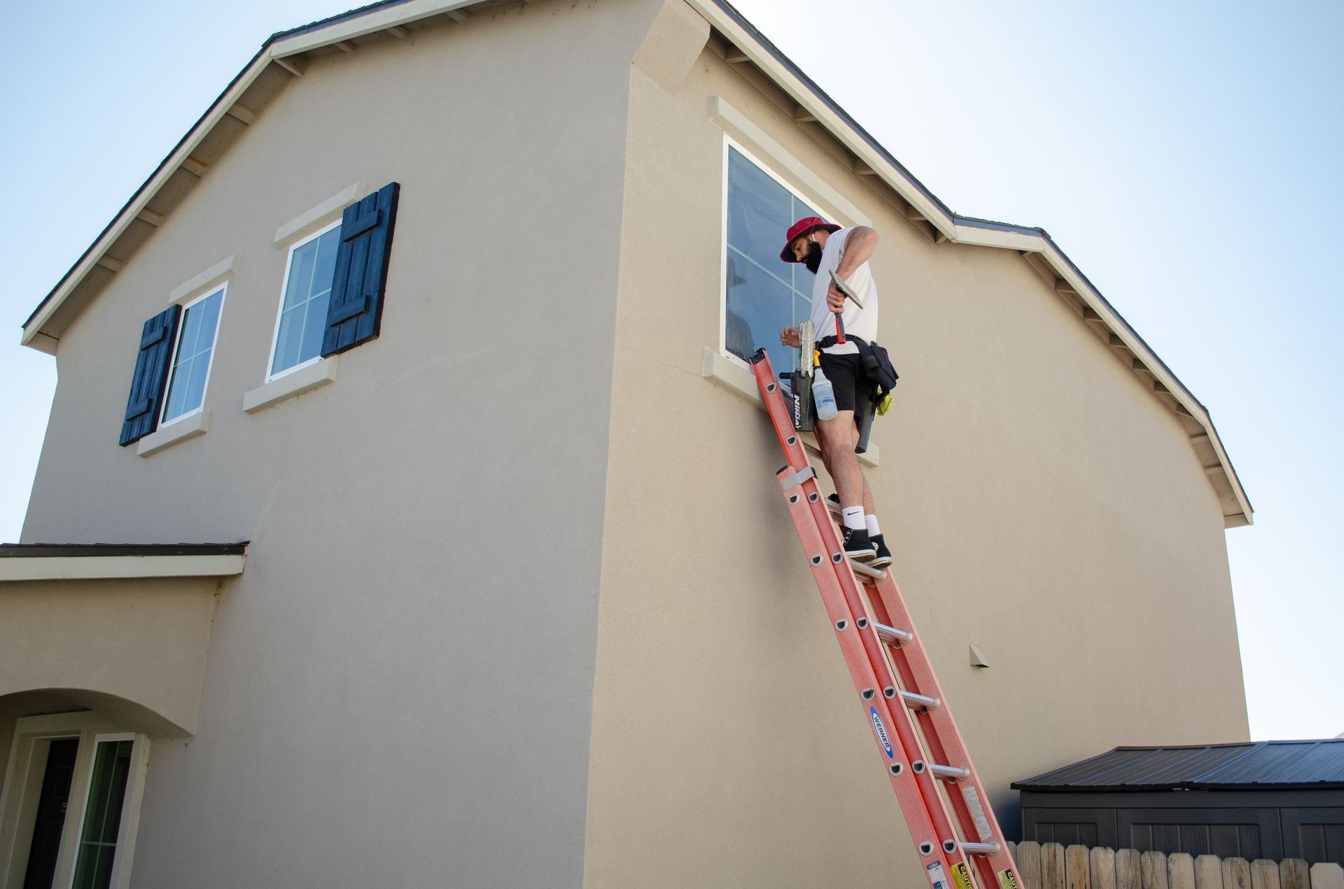 A man on a ladder is cleaning a window on the side of a house.