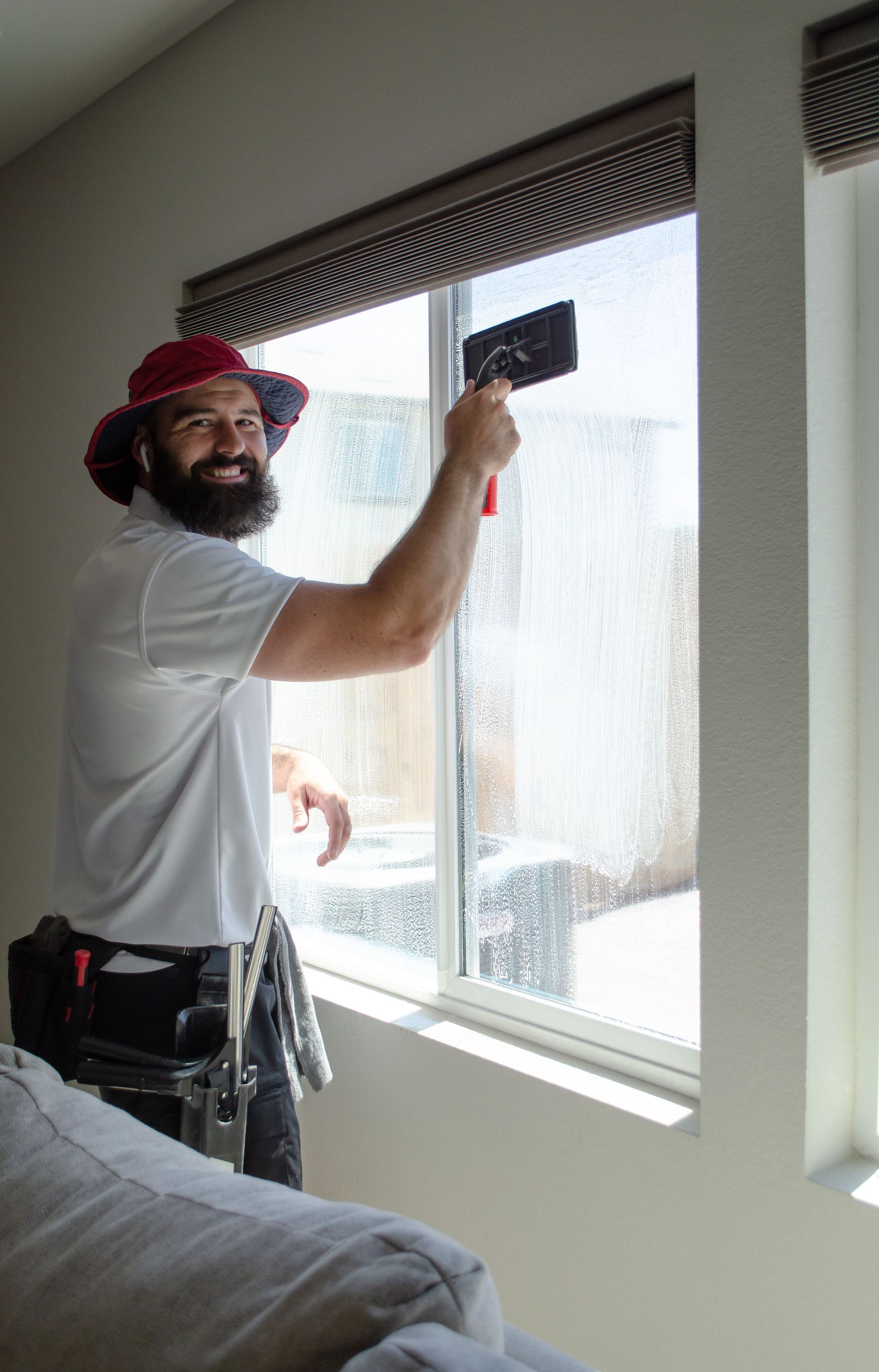A man is cleaning a window with a spatula in a living room.