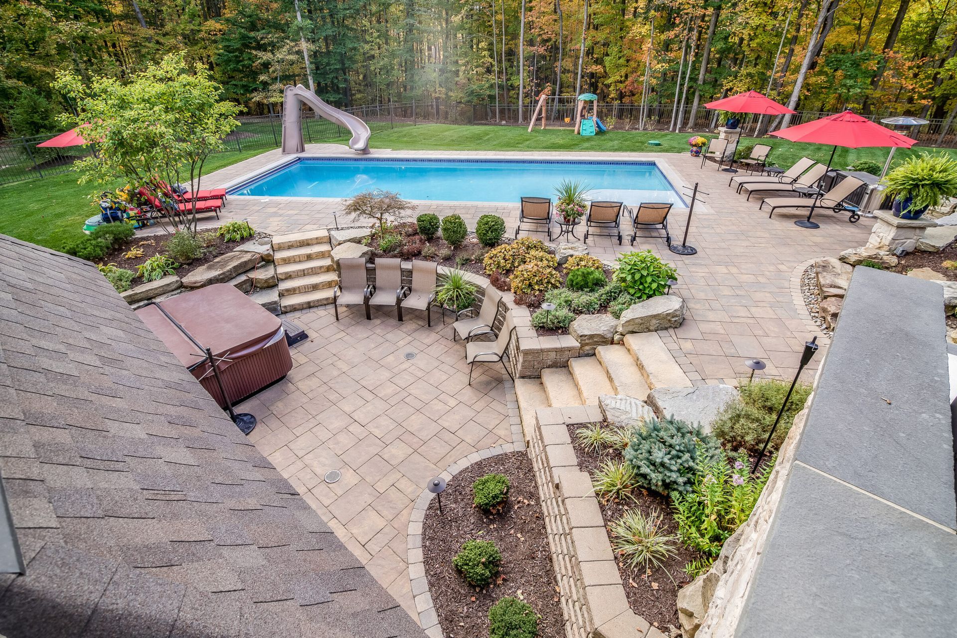 A large backyard stone patio with an inground pool and water slide.
