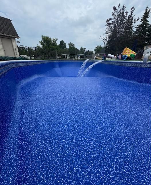 Blue pool filling with water, cloudy sky, residential setting.