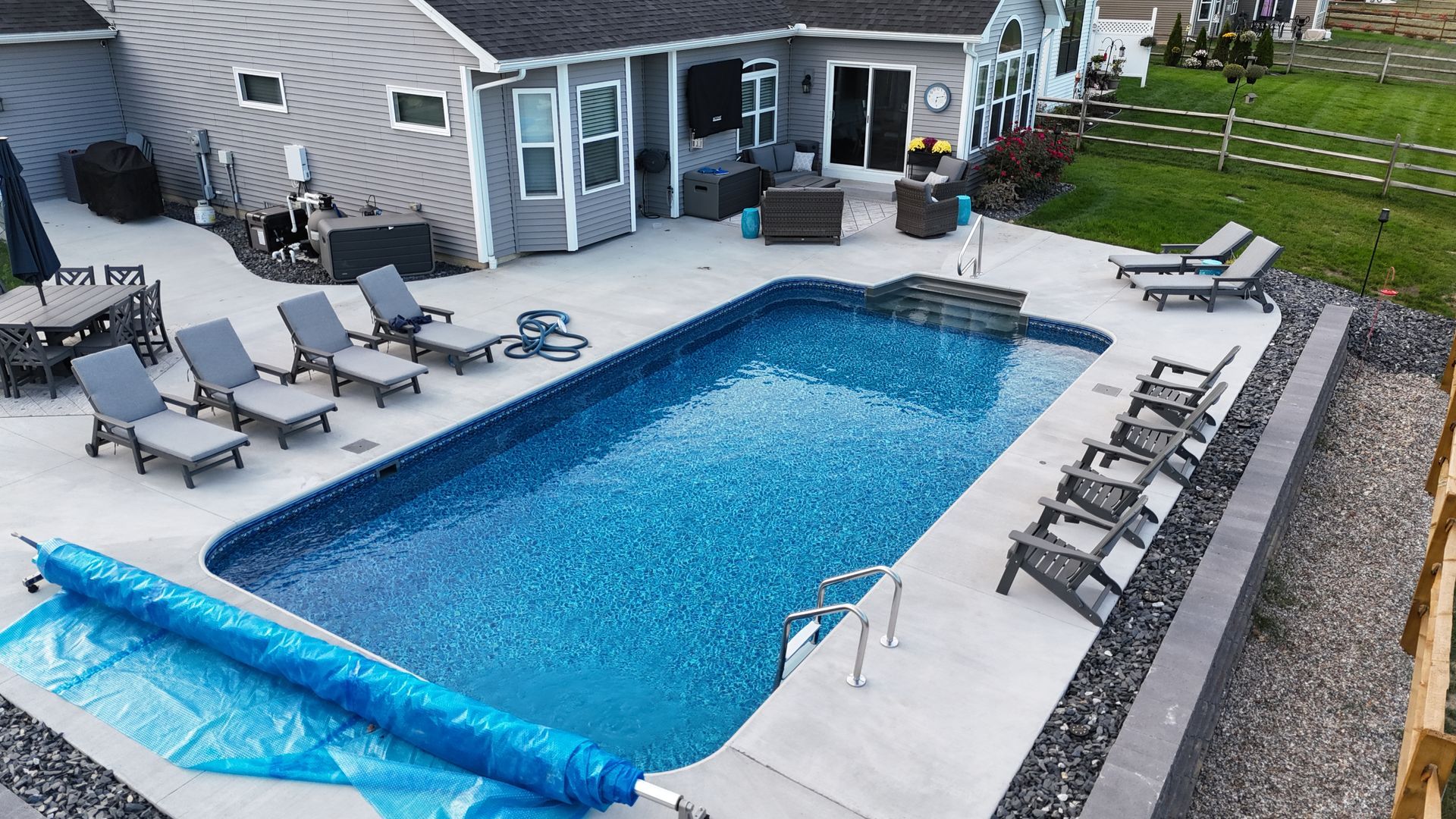 Backyard with rectangular pool, lounge chairs, patio furniture, and a house.