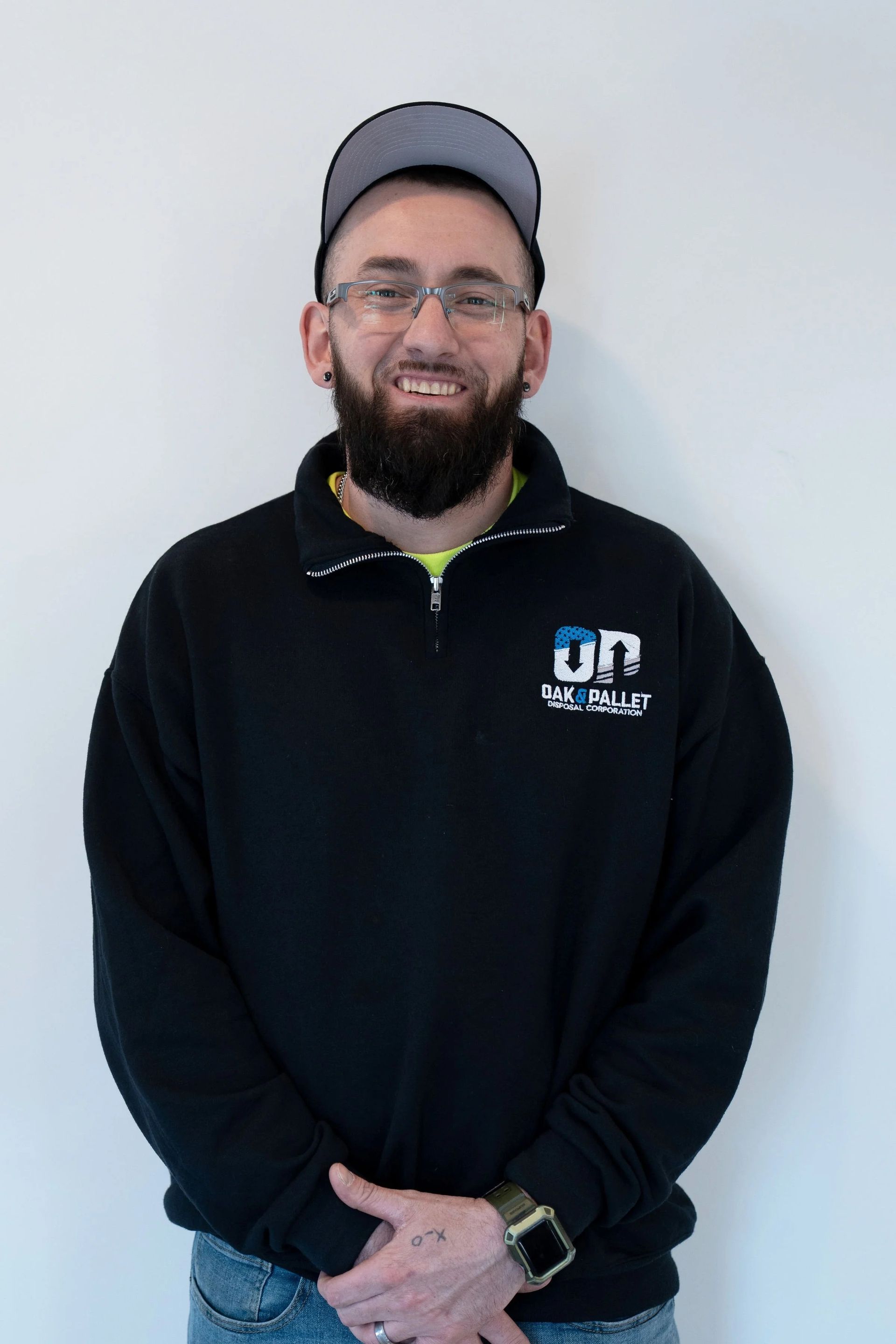 Man wearing a black hat and sweatshirt, with a beard, glasses, and a watch.