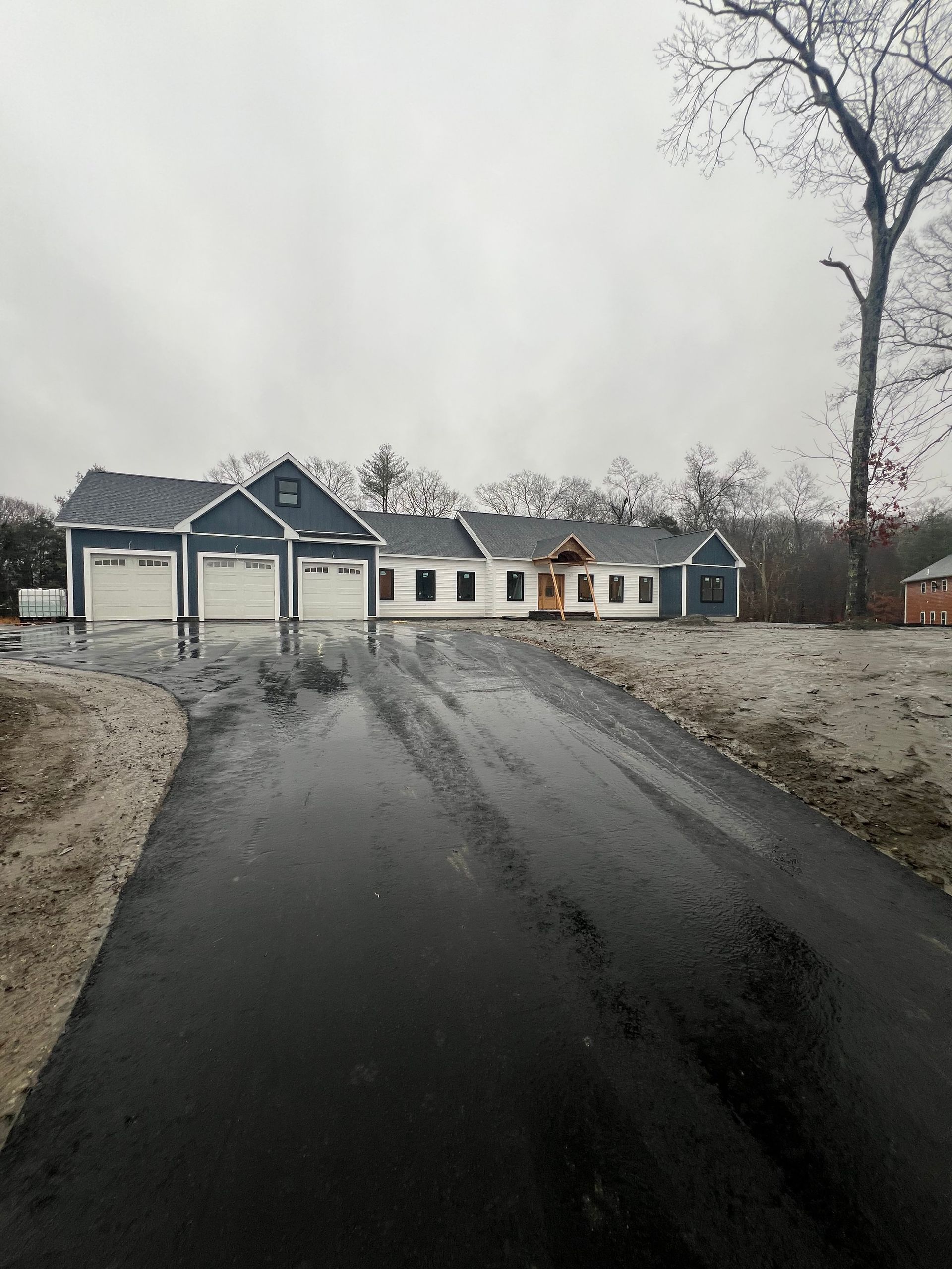 Newly constructed house with three-car garage, long asphalt driveway, cloudy sky.