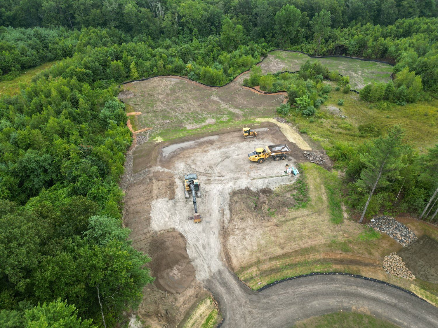 Construction site in a wooded area; heavy machinery, dirt piles, cleared land.