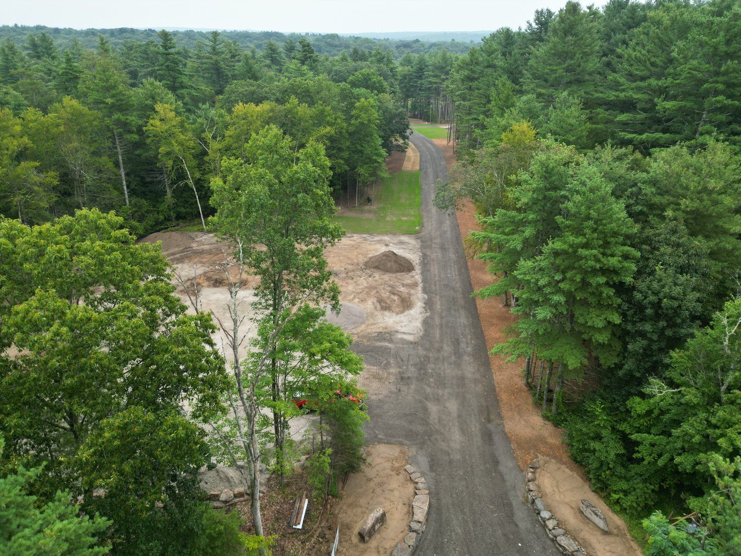 Gravel road through a forest with a cleared area on the left. Overcast day.