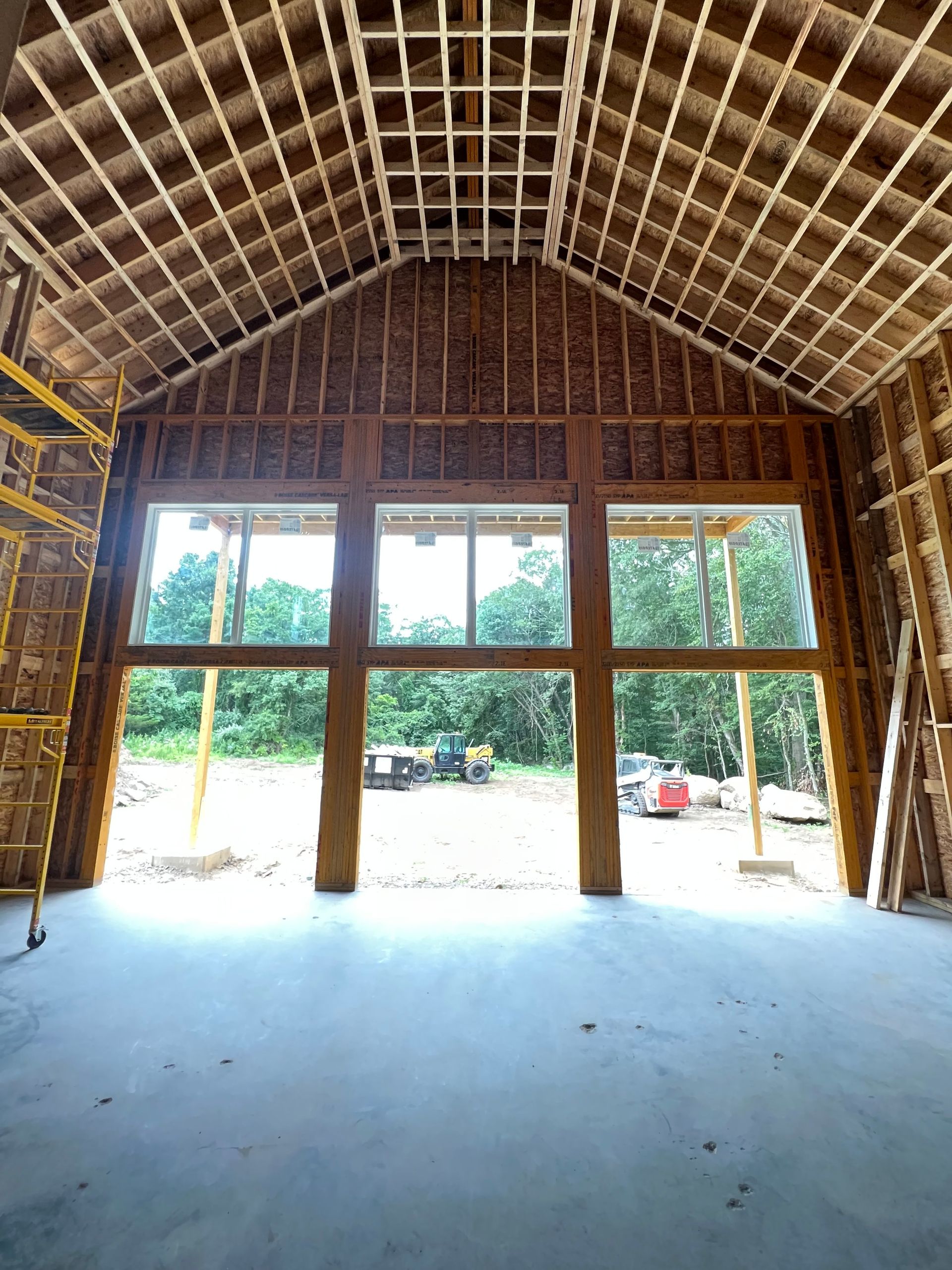 Interior view of a building under construction, featuring large windows and exposed wooden framework.