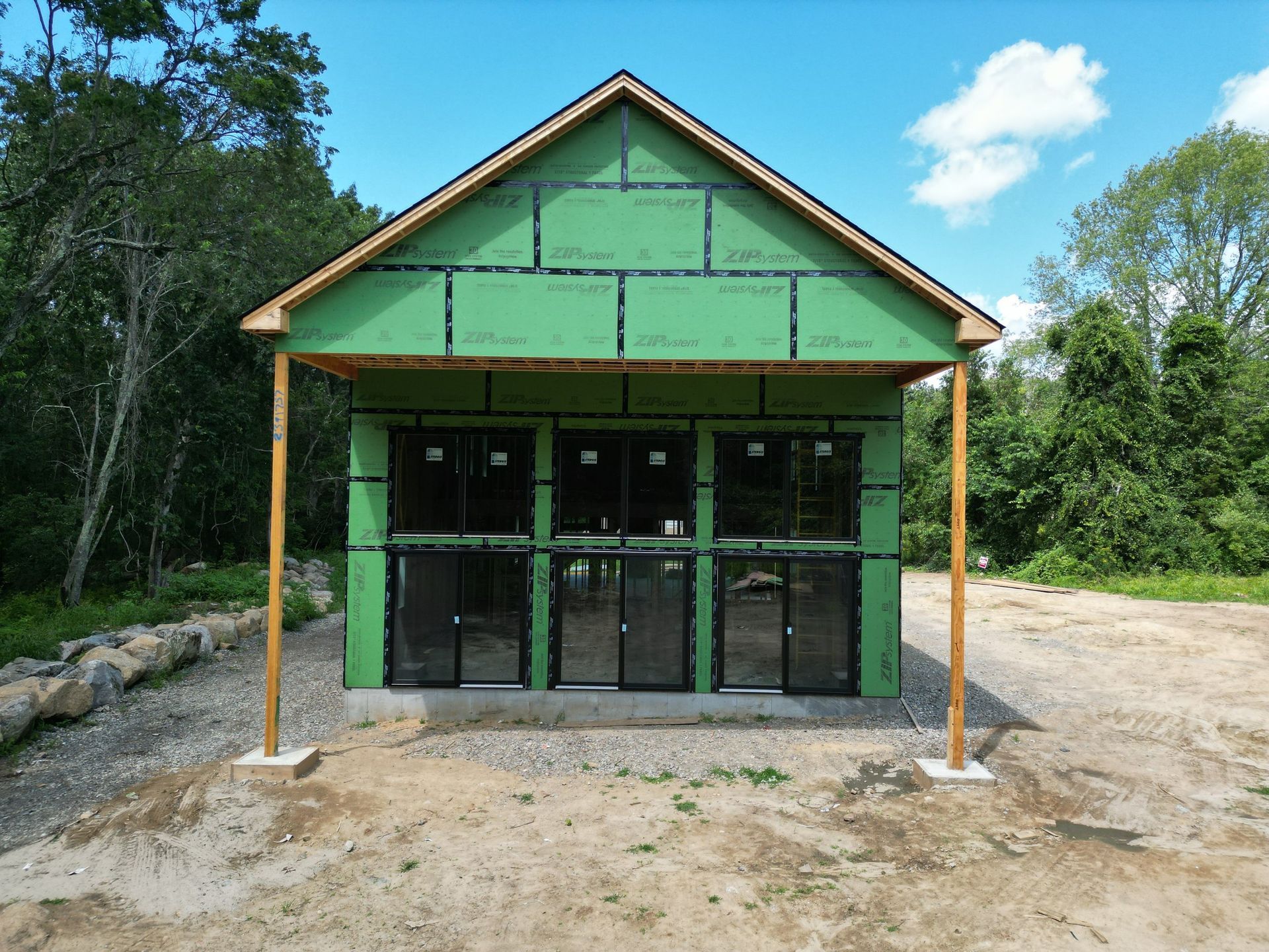 Green-sheathed building under construction, featuring multiple dark-framed windows, supported by wooden posts.