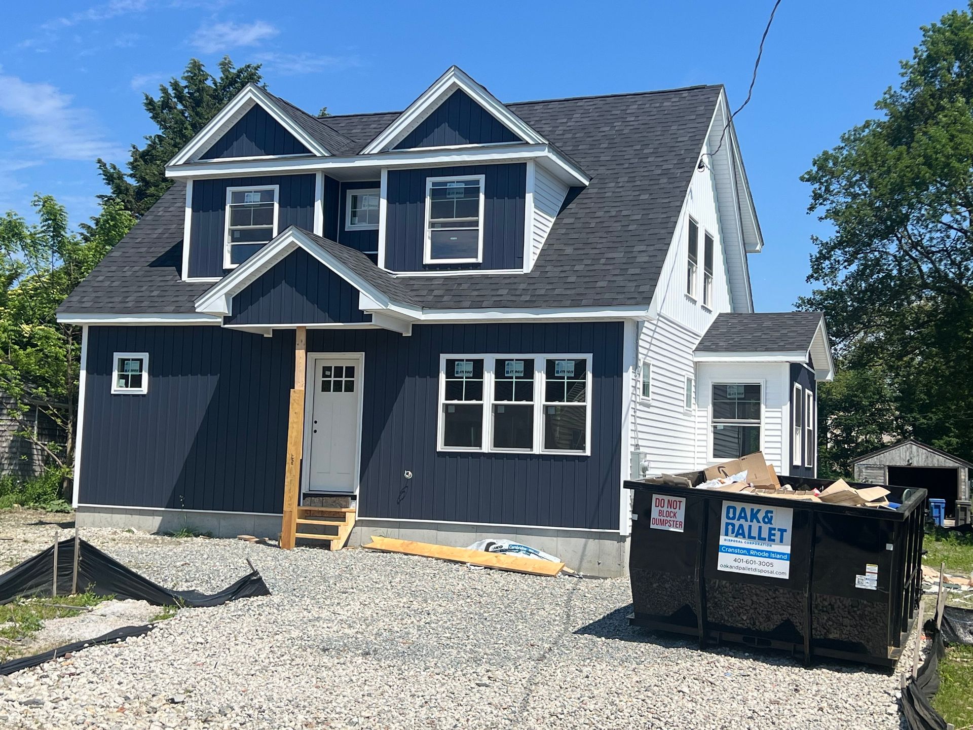 New house under construction with dark blue siding, white trim, and a dumpster.