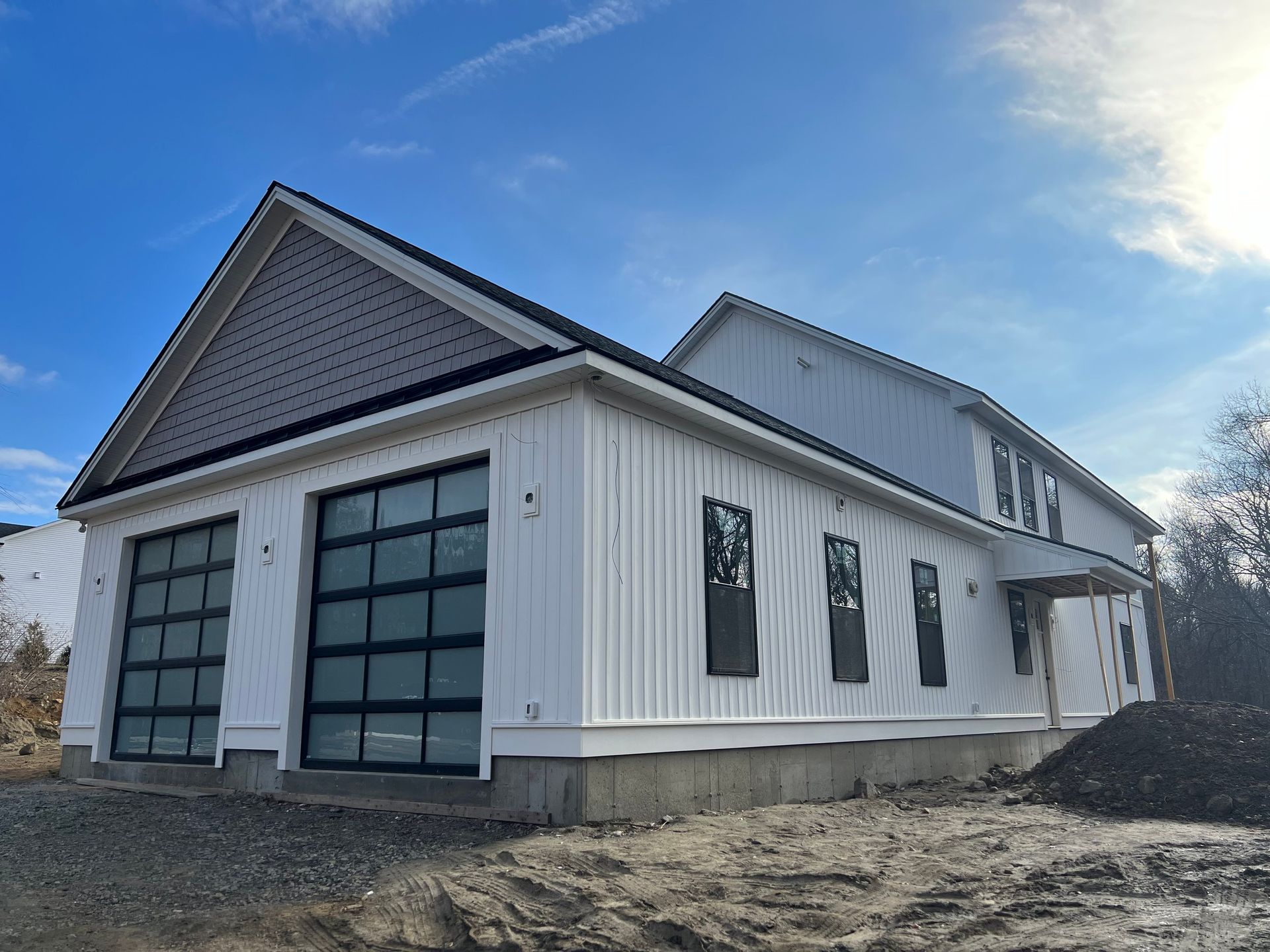 New house under construction with white siding, two garage doors with black frames, and clear glass.