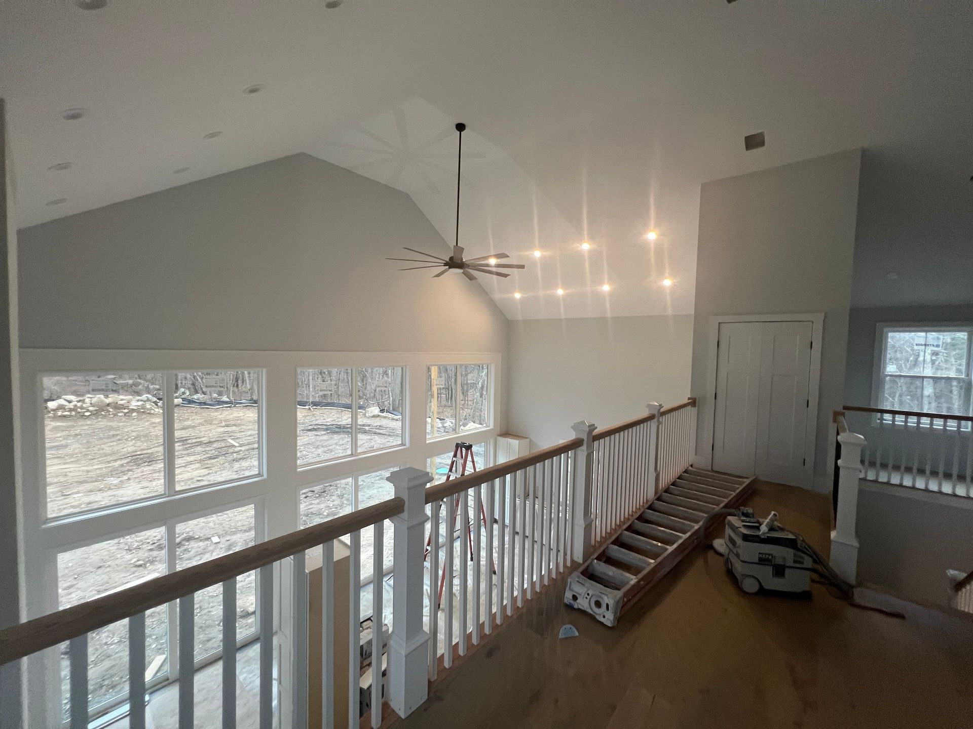 Interior view of a house with a high ceiling, windows, and a railing.