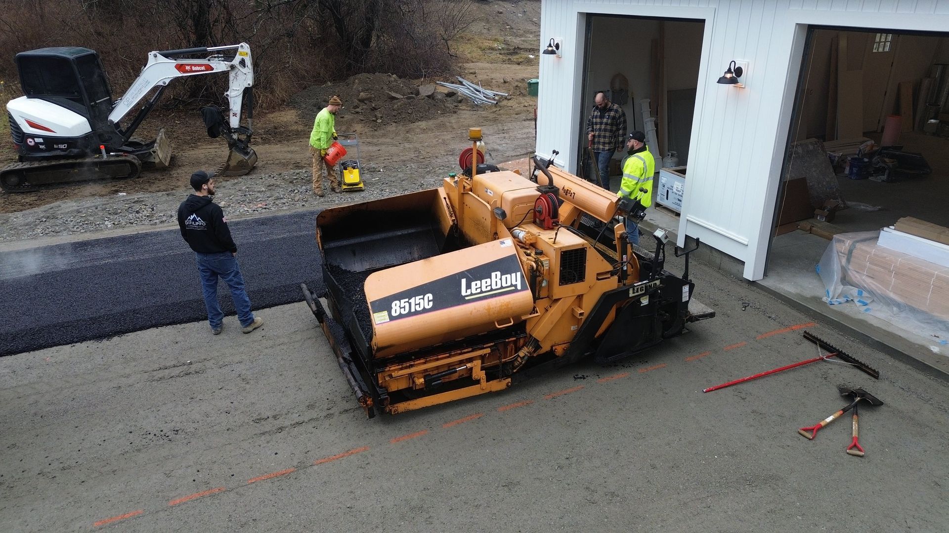 Construction workers paving a driveway with asphalt machine.
