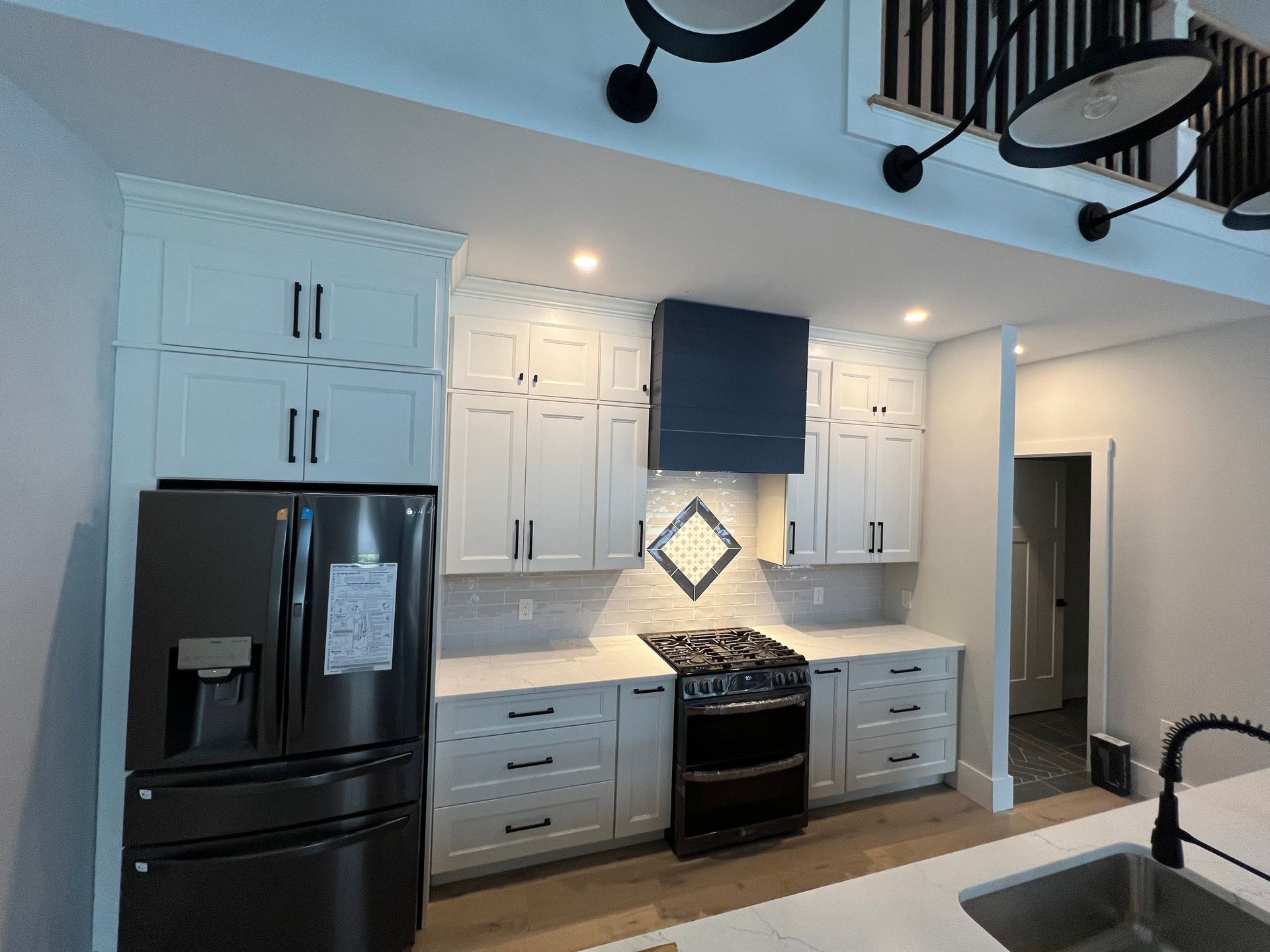 Kitchen with white cabinets, black appliances, navy range hood.